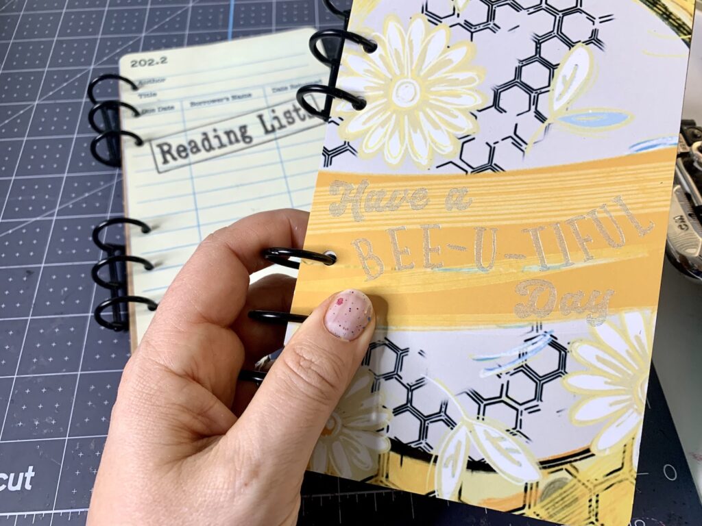 My hand holding an engraved sublimated notebook with a bee design